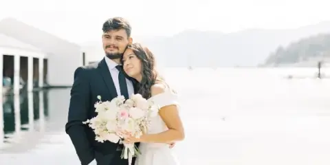 A bride and groom standing together, with the bride holding a large bouquet of white and pink flowers.