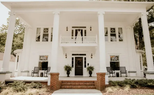 Front view of the white-columned historic manor at Sparrow Grove with a wedding dress hanging from the balcony.