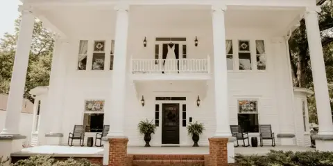 Front view of the white-columned historic manor at Sparrow Grove with a wedding dress hanging from the balcony.