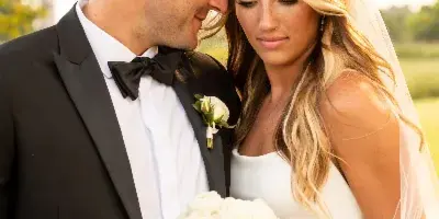A close-up portrait of a bride and groom in wedding attire, with the bride holding a white rose bouquet.