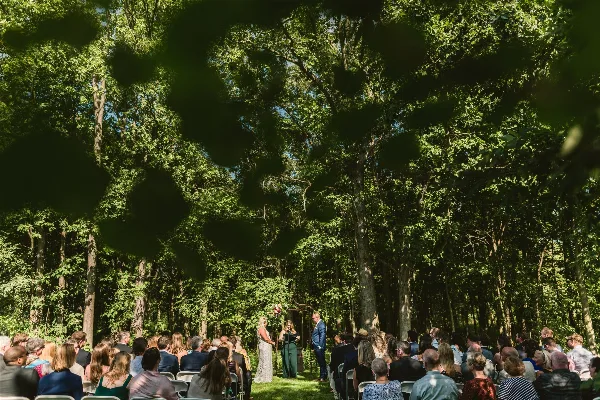 Outdoor wedding ceremony taking place in a forest clearing with seated guests.
