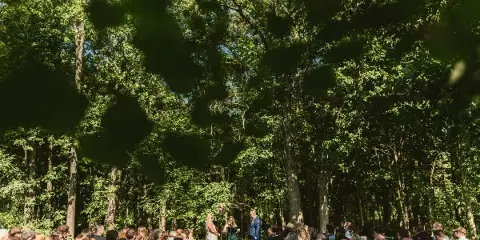 Outdoor wedding ceremony taking place in a forest clearing with seated guests.