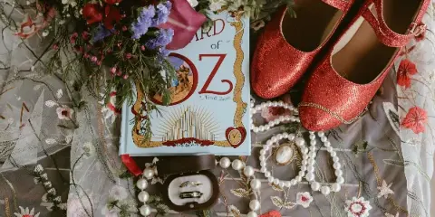 A flat lay photograph of a wedding dress, red sparkly shoes, a bouquet of flowers, a book, and wedding rings.