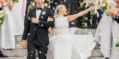 A bride and groom walking down stone steps with their wedding party while confetti falls around them.