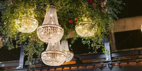 A suspended floral installation with chandeliers and a neon sign reading 'Ashley & C' at a wedding venue.