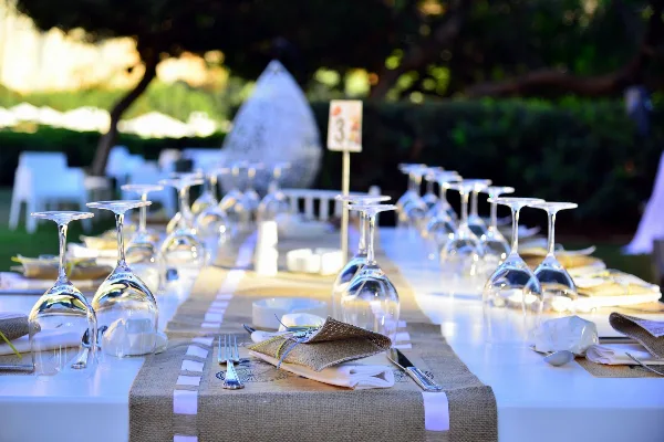 A close-up view of a decorated event table featuring a burlap runner, white linens, and inverted wine glasses.