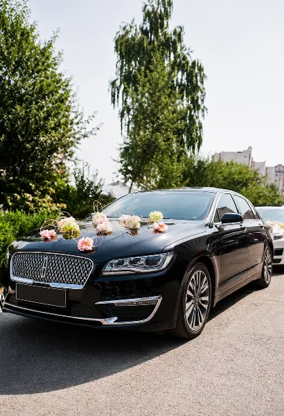 A black luxury sedan decorated with pink and white flowers on the hood, parked outdoors.