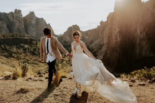 A bride and groom holding hands while walking through a rocky, mountainous landscape.