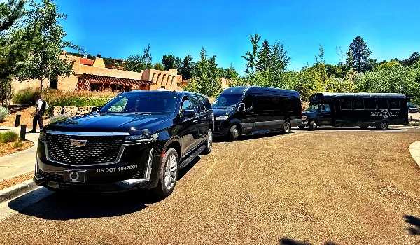 A lineup of Santa Fe Valet transportation vehicles including a black SUV, a passenger van, and a motor coach parked on a gravel lot.