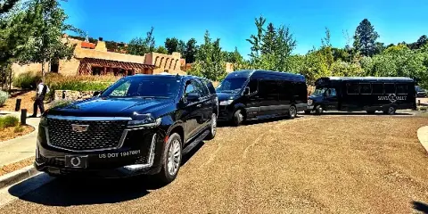 A lineup of Santa Fe Valet transportation vehicles including a black SUV, a passenger van, and a motor coach parked on a gravel lot.