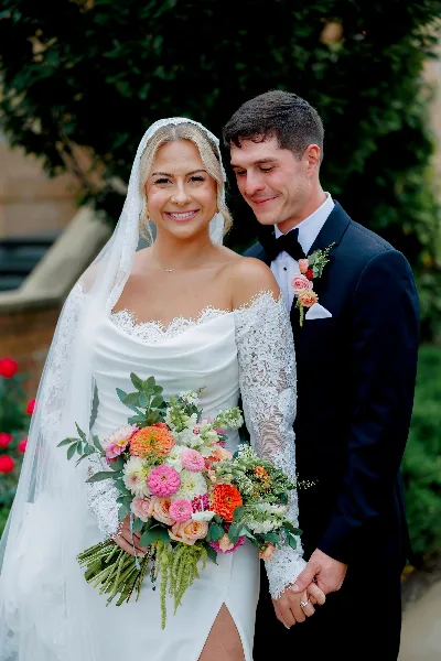 A bride and groom posing together, with the bride holding a colorful, garden-inspired wedding bouquet.