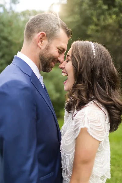A bride and groom smiling at each other outdoors in a field.