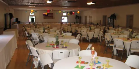 Interior of a large community hall set up for an event with round tables and white chairs.