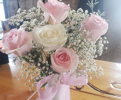 Pink and white rose bouquet with baby's breath tied with a pink ribbon on a wooden table