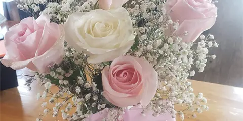 Pink and white rose bouquet with baby's breath tied with a pink ribbon on a wooden table