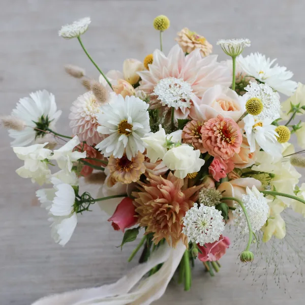 A garden-style wedding bouquet featuring white daisies, pink dahlias, and roses with a white ribbon.
