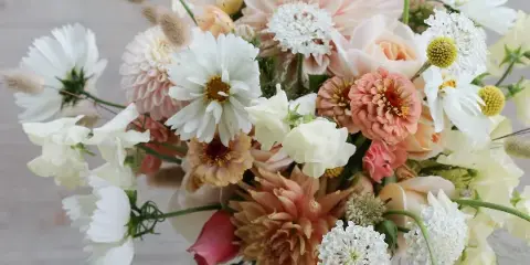 A garden-style wedding bouquet featuring white daisies, pink dahlias, and roses with a white ribbon.