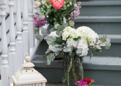 A white floral arrangement in a glass vase and a white lantern placed on a grey staircase with white balusters.