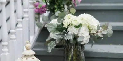 A white floral arrangement in a glass vase and a white lantern placed on a grey staircase with white balusters.