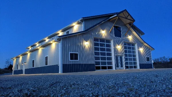 Exterior view of a large metal barn event venue with illuminated exterior lights at dusk.