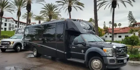 A black MIB Transportation 28-passenger shuttle bus parked outdoors with palm trees in the background.