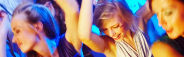 A group of people dancing at a party or event under blue and purple lighting.