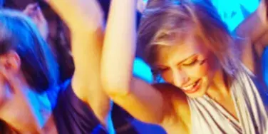 A group of people dancing at a party or event under blue and purple lighting.