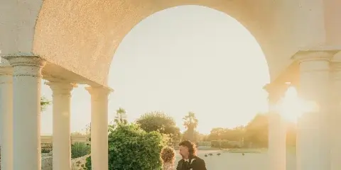A bride and groom standing together under a white stone archway during a wedding photoshoot.