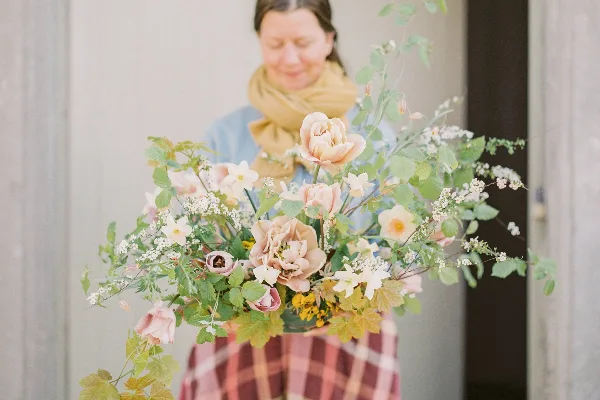 A person holding a large, loose floral arrangement with pink and cream flowers and greenery.