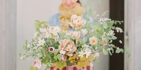 A person holding a large, loose floral arrangement with pink and cream flowers and greenery.