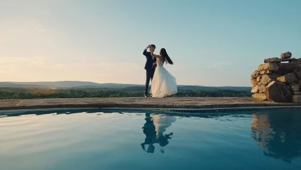 A bride and groom dancing by a pool at sunset.