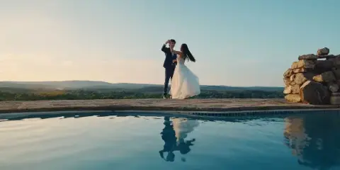 A bride and groom dancing by a pool at sunset.