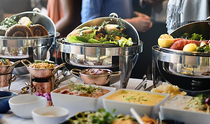 A catering buffet table featuring multiple stainless steel chafing dishes filled with salads, meats, and other prepared foods.