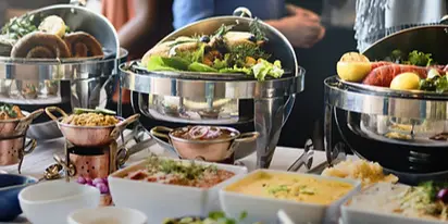 A catering buffet table featuring multiple stainless steel chafing dishes filled with salads, meats, and other prepared foods.