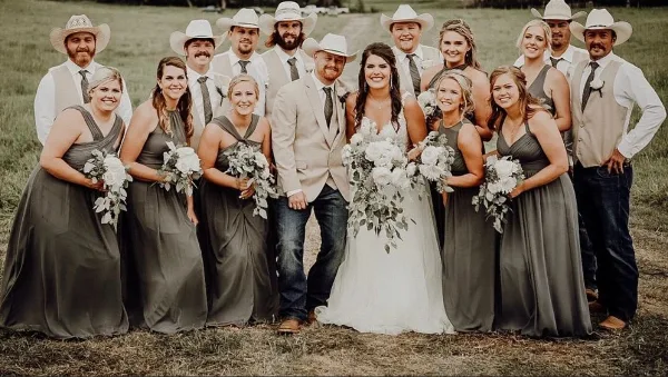 A wedding party posing outdoors with white floral bouquets and a large bridal bouquet.
