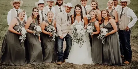A wedding party posing outdoors with white floral bouquets and a large bridal bouquet.