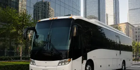 A white and black motorcoach bus parked on a city street in front of modern glass buildings.