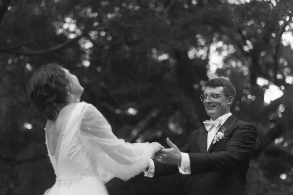 A black and white photograph of a bride and groom dancing together outdoors.