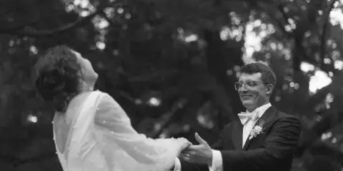 A black and white photograph of a bride and groom dancing together outdoors.