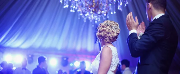 A bride and groom dancing at a wedding reception under blue stage lighting and a chandelier.