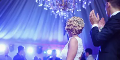A bride and groom dancing at a wedding reception under blue stage lighting and a chandelier.