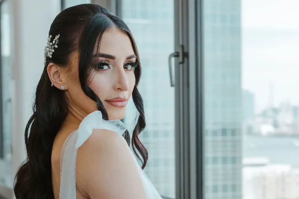 A bride with professional makeup and styled hair looking over her shoulder.