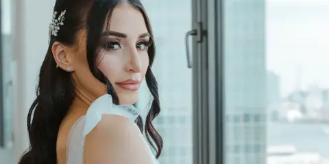 A bride with professional makeup and styled hair looking over her shoulder.
