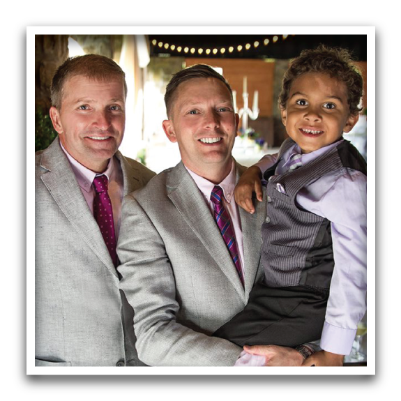 Two men in suits and a young boy in a vest smiling together at an event.