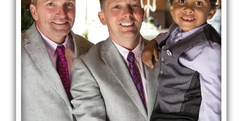 Two men in suits and a young boy in a vest smiling together at an event.