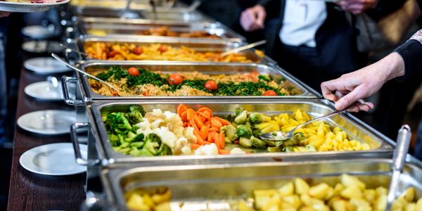 A catering buffet line featuring various food items in metal chafing dishes with a server serving guests.