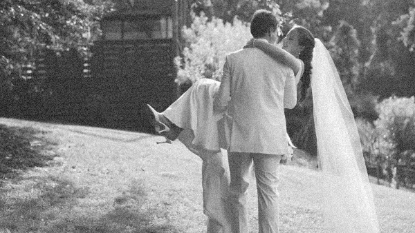 A black and white photograph of a groom lifting a bride in a garden setting.
