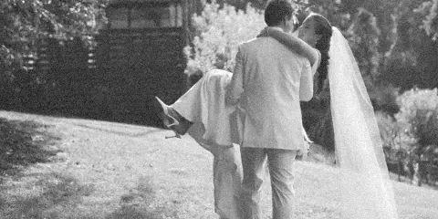 A black and white photograph of a groom lifting a bride in a garden setting.
