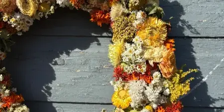 A large, lush floral wreath with orange, yellow, and white flowers hanging on a weathered blue wooden door.