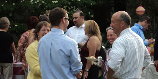 A group of people socializing at an outdoor event, holding plates of food and drinks.